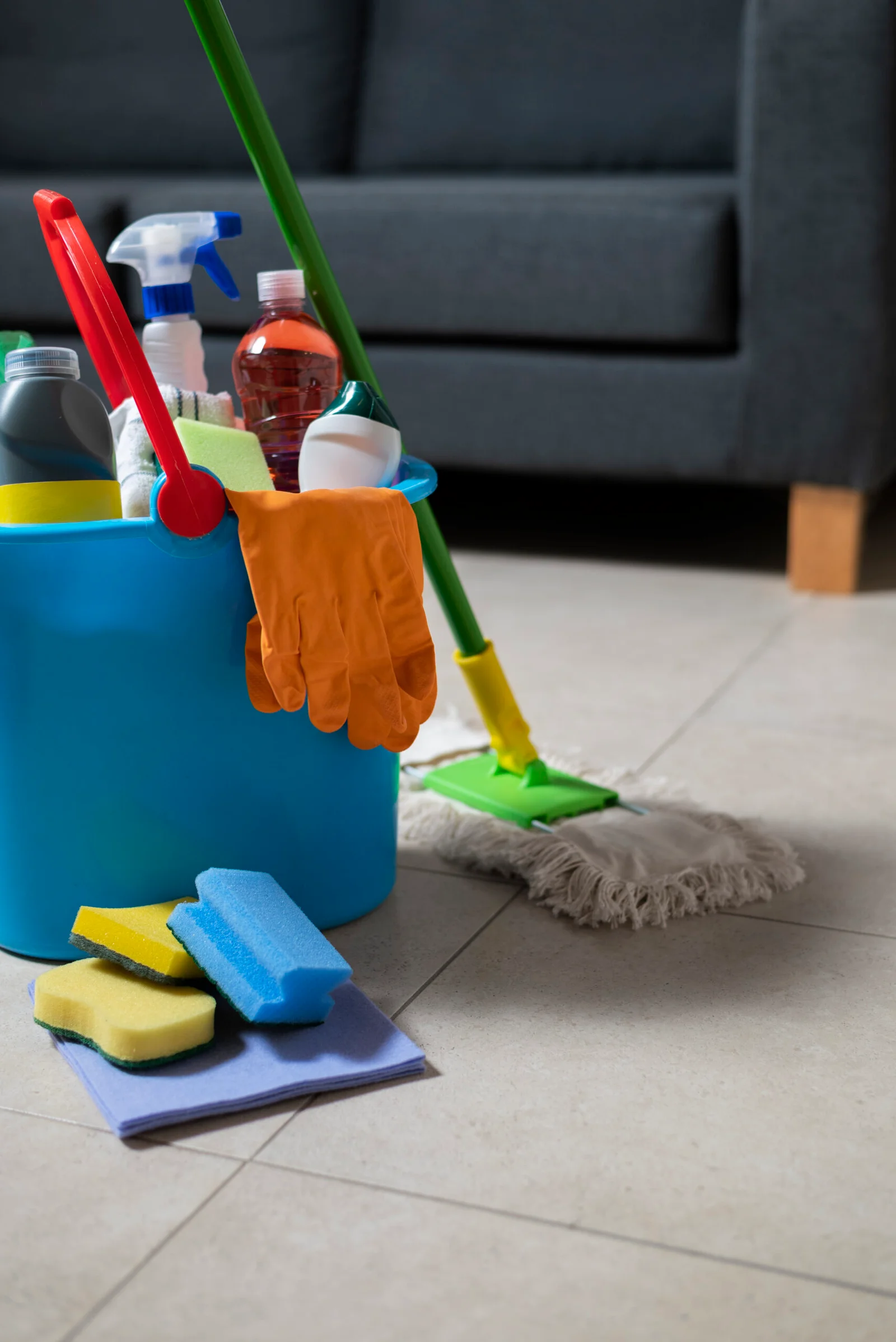 Cleaning supplies in a bucket on the floor, including spray bottles, sponges, and gloves at Golden